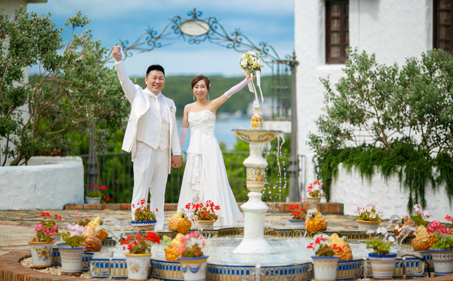 志摩地中海村　噴水前にて　手を振る白いドレス姿の新婦と白いタキシードの新郎