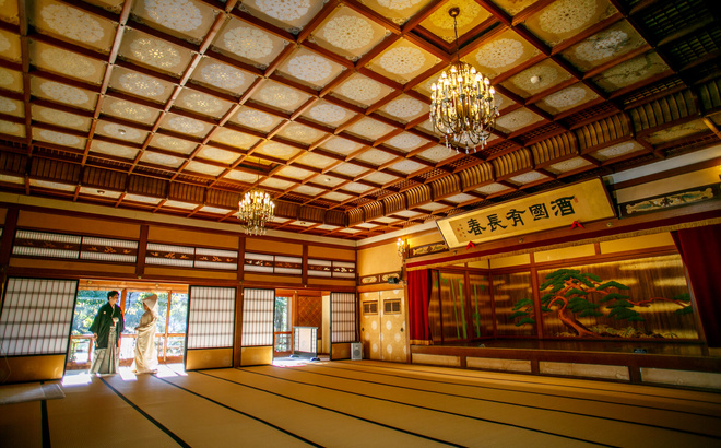賓日館大広間全景の中にたたずむ新郎新婦