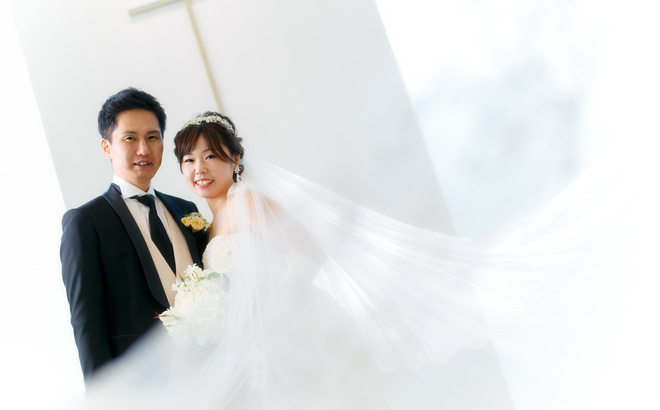 鳥羽国際ホテルチャペル内にて ベールがふわりとする中で黒いタキシードの新郎と白いドレスの新婦